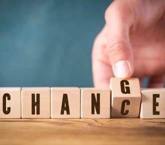 male hand flipping one of six cubes with letters, turning the word "change" to "chance". Cubes are lying on wooden surface.