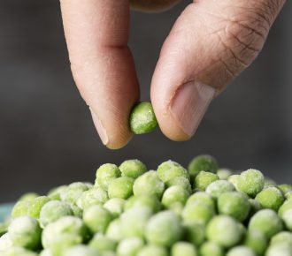 closeup of a man picking a green pea from a pile of frozen green peas